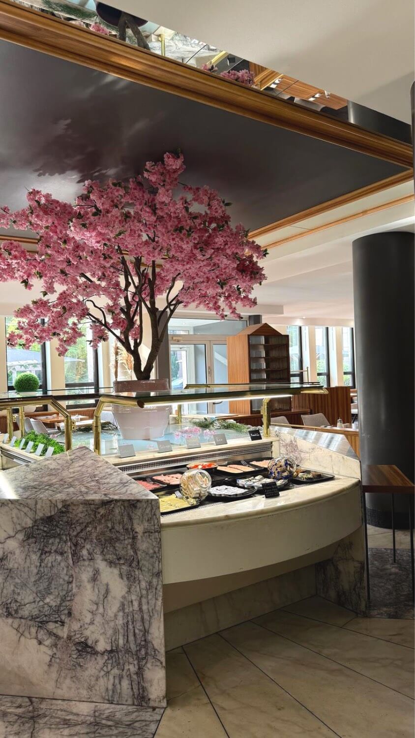 Breakfast buffet counter with pink tree and restaurant seating.
